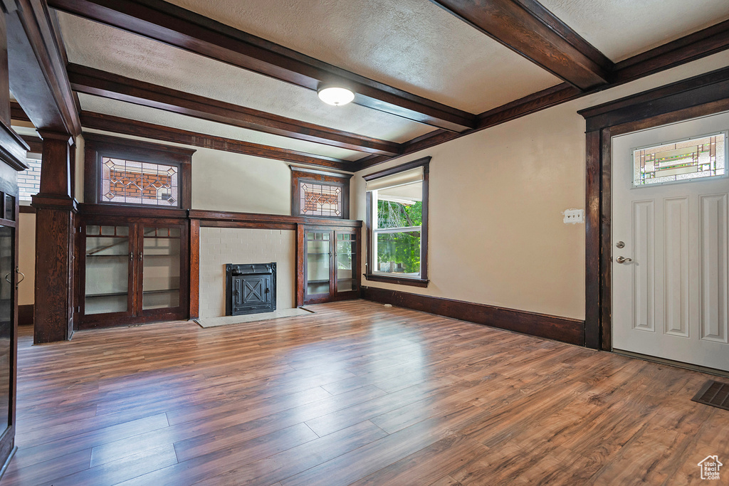 Unfurnished living room featuring beam ceiling, a textured ceiling, and wood-type flooring