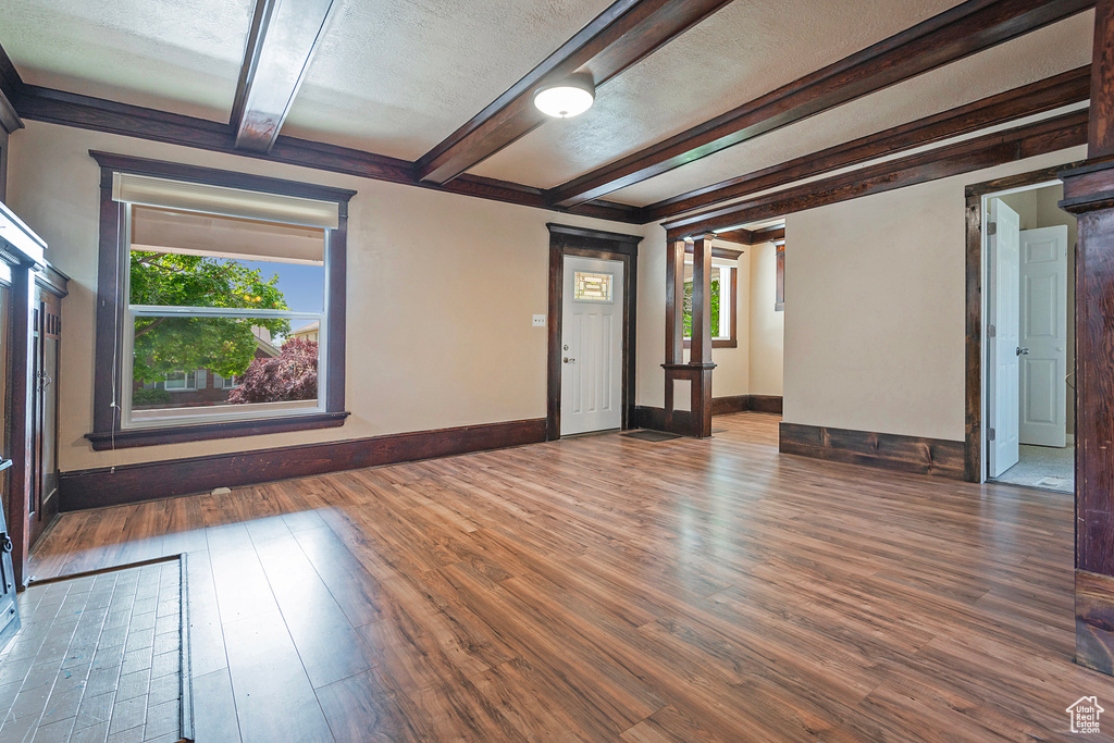 Unfurnished living room featuring a textured ceiling, plenty of natural light, beam ceiling, and dark hardwood / wood-style floors