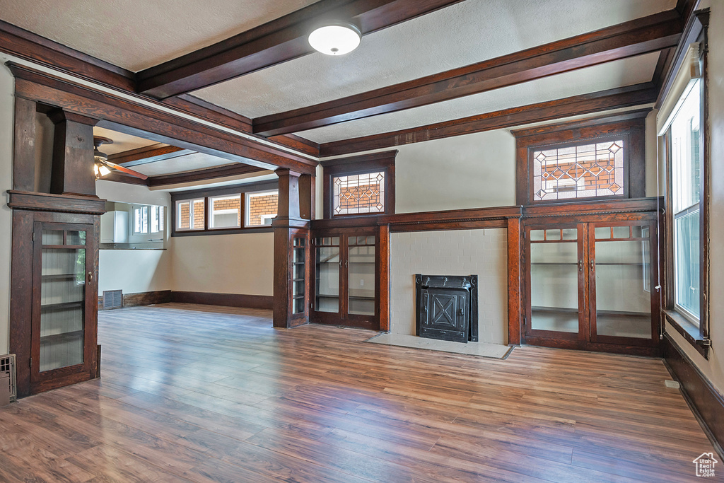 Unfurnished living room featuring beamed ceiling, plenty of natural light, ceiling fan, and dark hardwood / wood-style floors