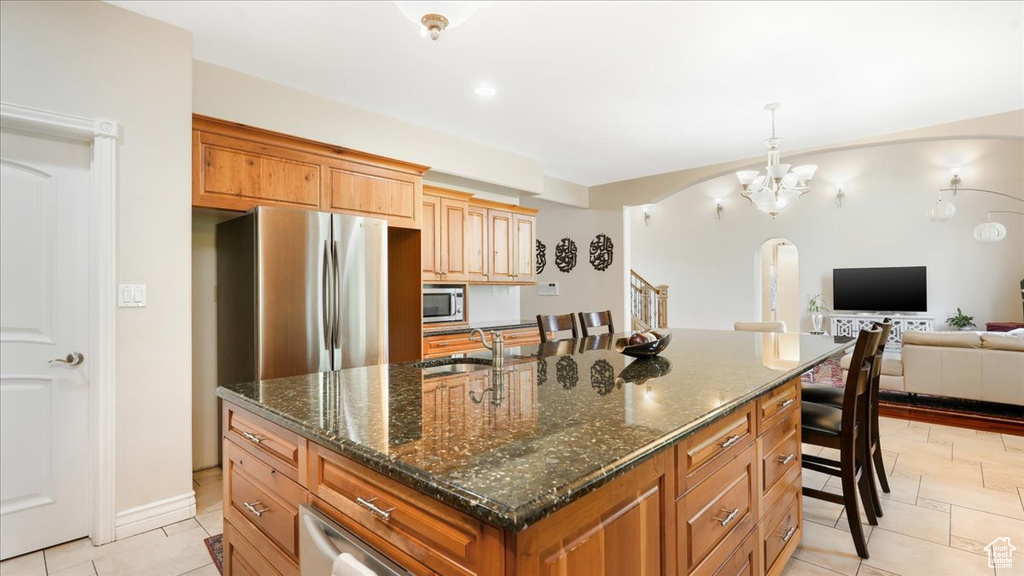 Kitchen with dark stone counters, light tile flooring, sink, a kitchen island with sink, and a chandelier