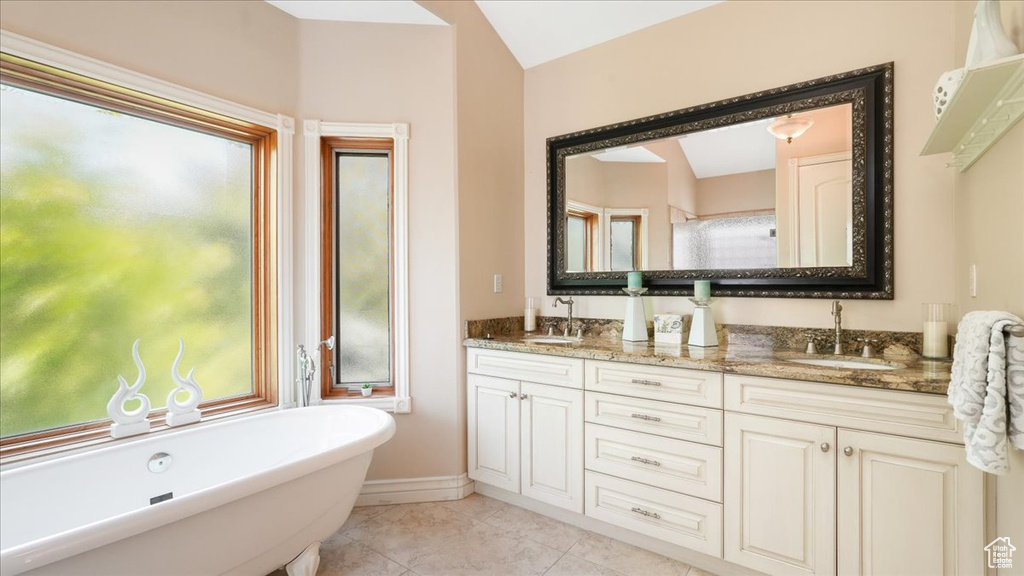 Bathroom featuring tile floors, dual sinks, vanity with extensive cabinet space, and a bath to relax in