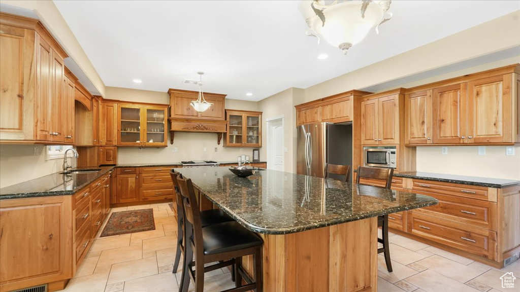 Kitchen with a kitchen island, stainless steel appliances, dark stone counters, a breakfast bar, and light tile floors