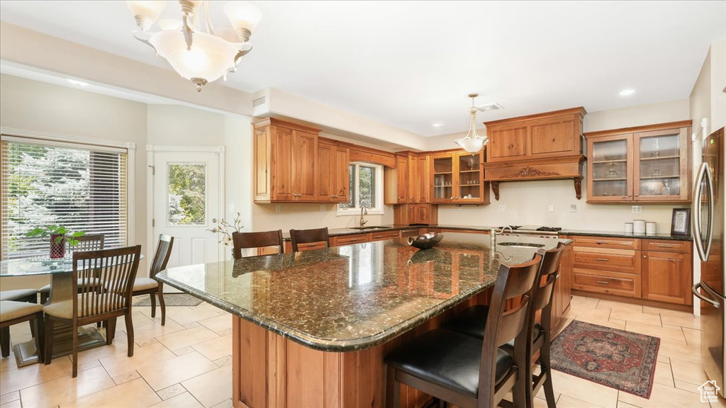 Kitchen featuring custom exhaust hood, decorative light fixtures, dark stone countertops, light tile floors, and a center island