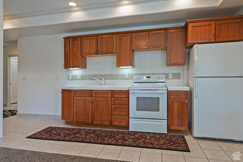 Kitchen with backsplash, ornamental molding, sink, white appliances, and light tile floors