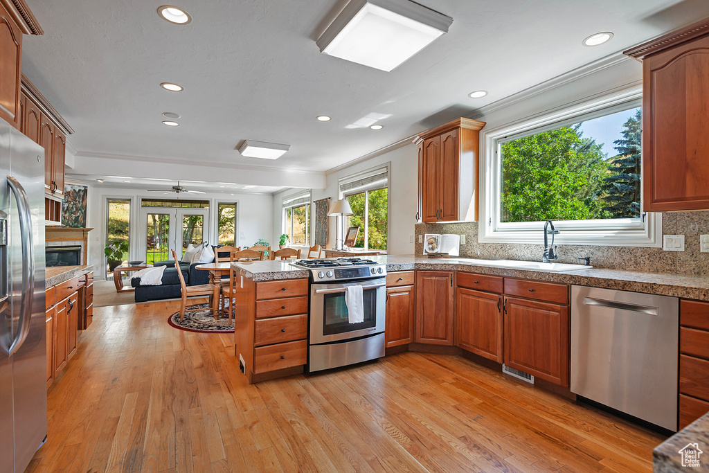 Kitchen with ceiling fan, light hardwood / wood-style flooring, kitchen peninsula, stainless steel appliances, and backsplash