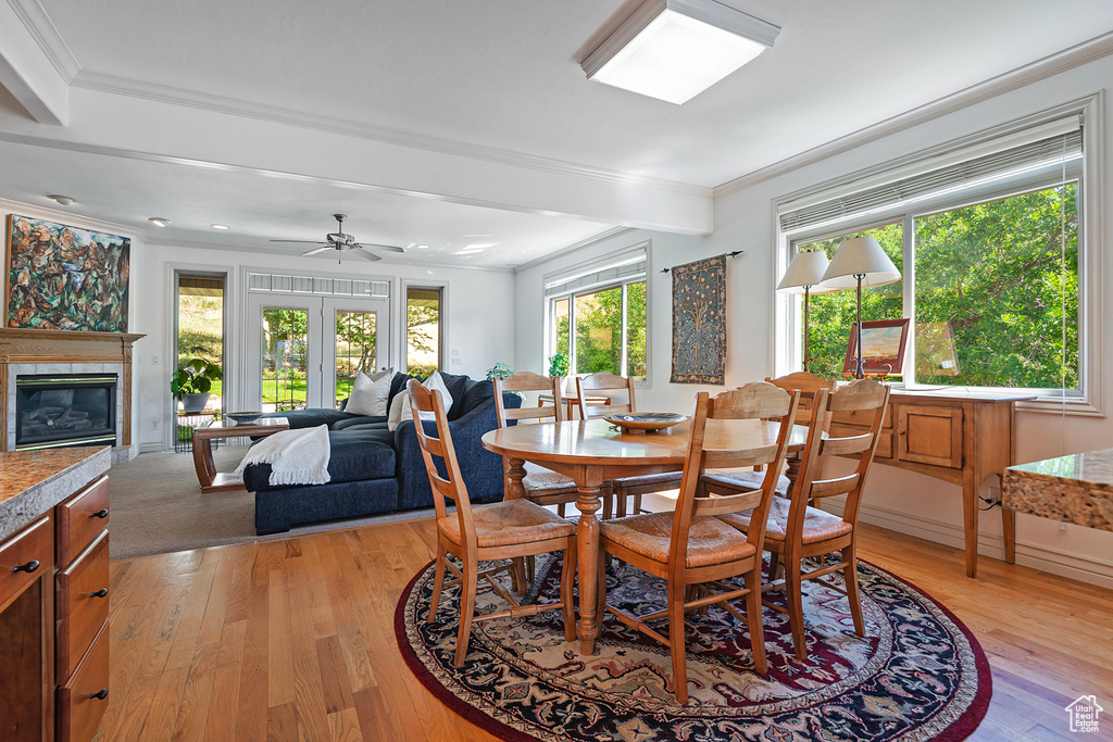 Dining space with a fireplace, ceiling fan, ornamental molding, light wood-type flooring, and french doors