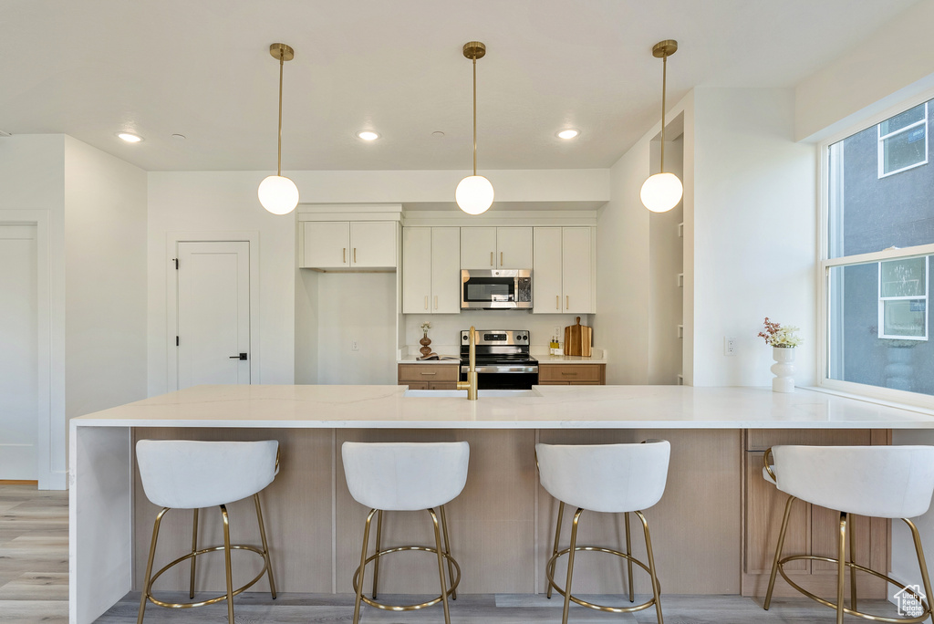 Kitchen featuring white cabinetry, stainless steel appliances, hanging light fixtures, and light wood-type flooring