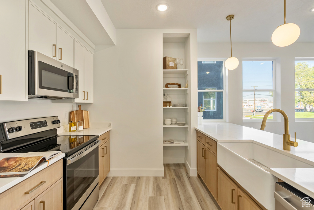 Kitchen with white cabinets, light wood-type flooring, stainless steel appliances, sink, and decorative light fixtures