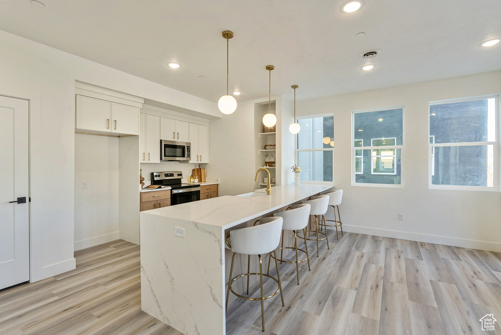 Kitchen featuring light stone counters, appliances with stainless steel finishes, white cabinetry, light wood-type flooring, and decorative light fixtures