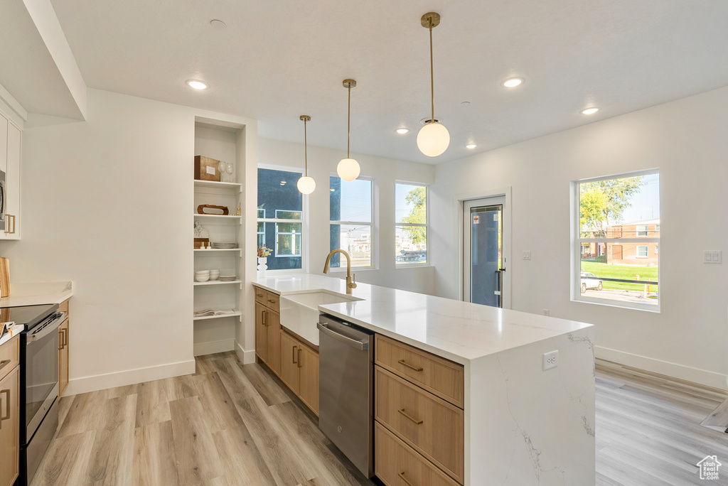 Kitchen with appliances with stainless steel finishes, light brown cabinetry, pendant lighting, light hardwood / wood-style floors, and sink