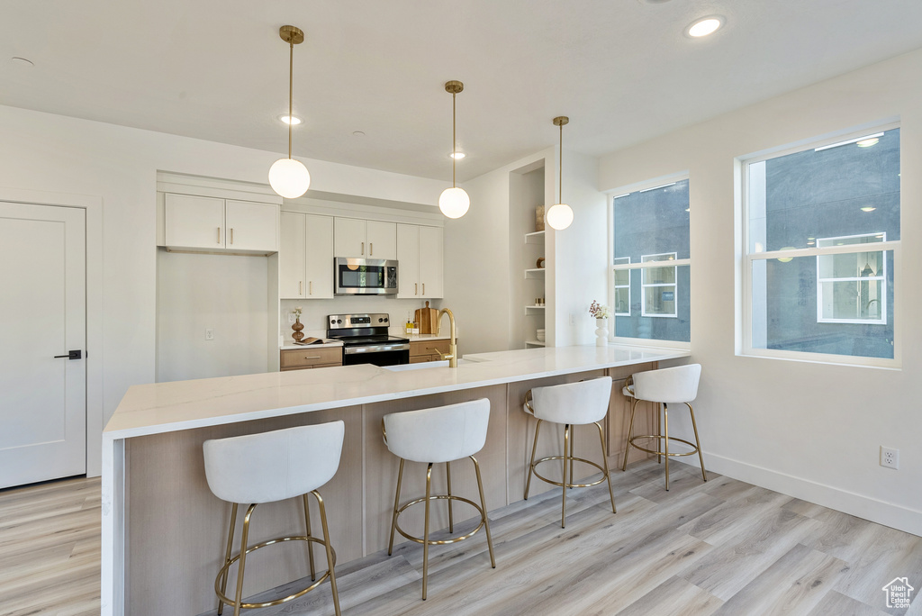 Kitchen featuring white cabinets, hanging light fixtures, stainless steel appliances, and light wood-type flooring