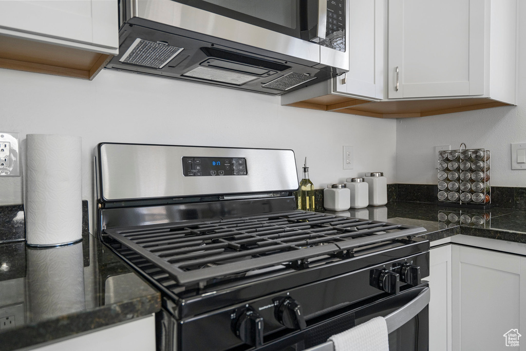 Kitchen featuring dark stone countertops, stainless steel appliances, and white cabinetry