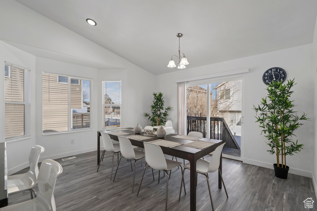 Dining room with dark wood-type flooring, a notable chandelier, and vaulted ceiling