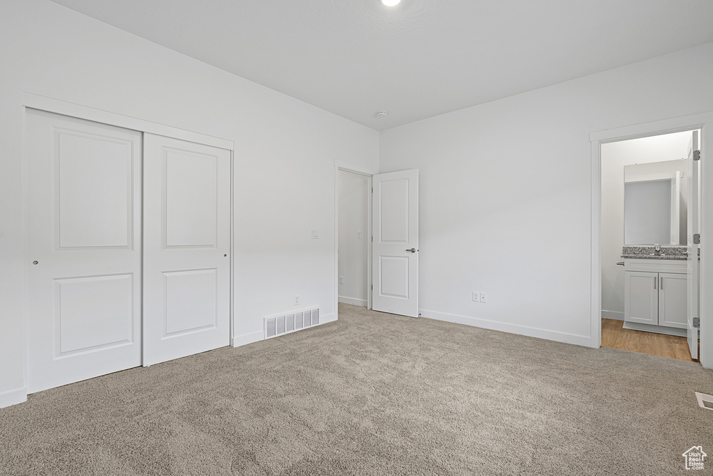 Unfurnished bedroom featuring ensuite bath, a closet, and light colored carpet