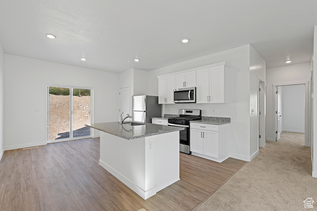 Kitchen with white cabinets, light hardwood / wood-style floors, stainless steel appliances, a center island with sink, and sink