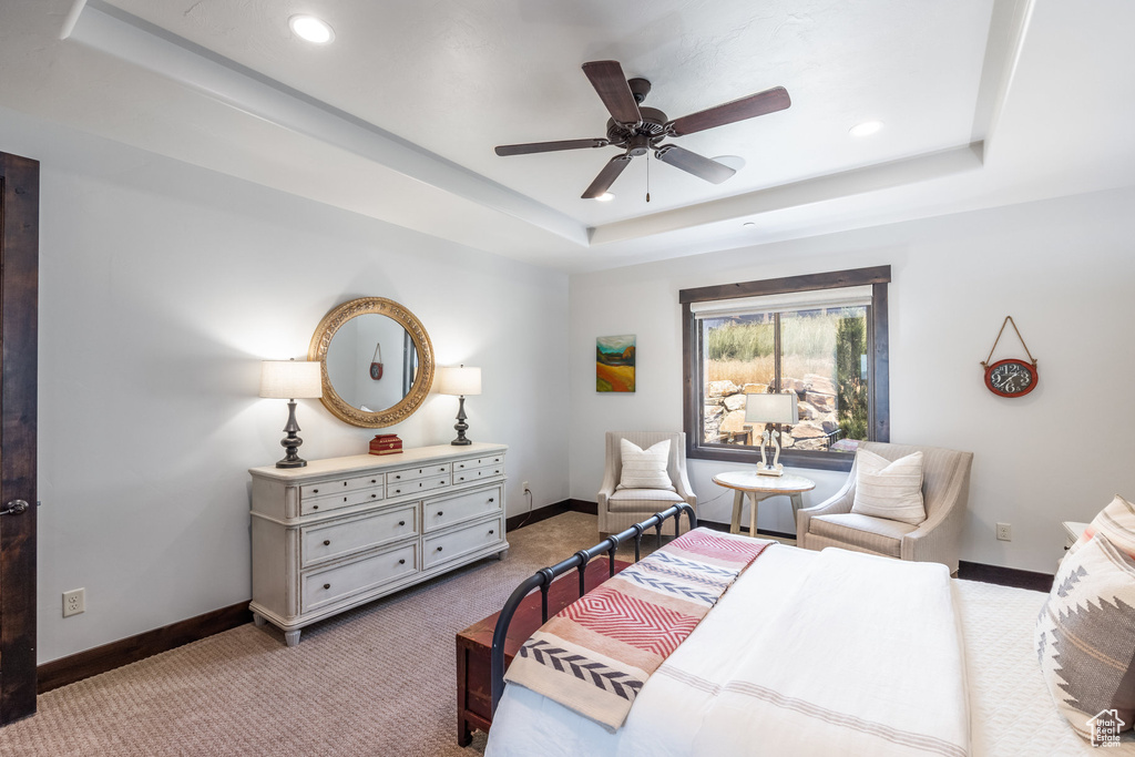 Bedroom with light colored carpet, ceiling fan, and a tray ceiling