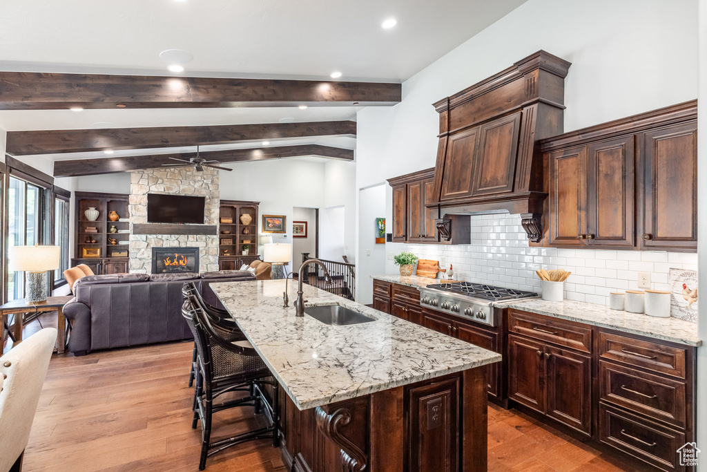 Kitchen with a stone fireplace, ceiling fan, light hardwood / wood-style floors, a center island with sink, and sink