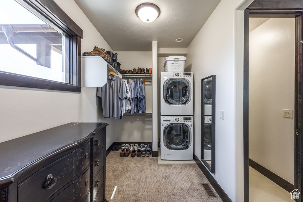 Washroom featuring stacked washing maching and dryer and light colored carpet