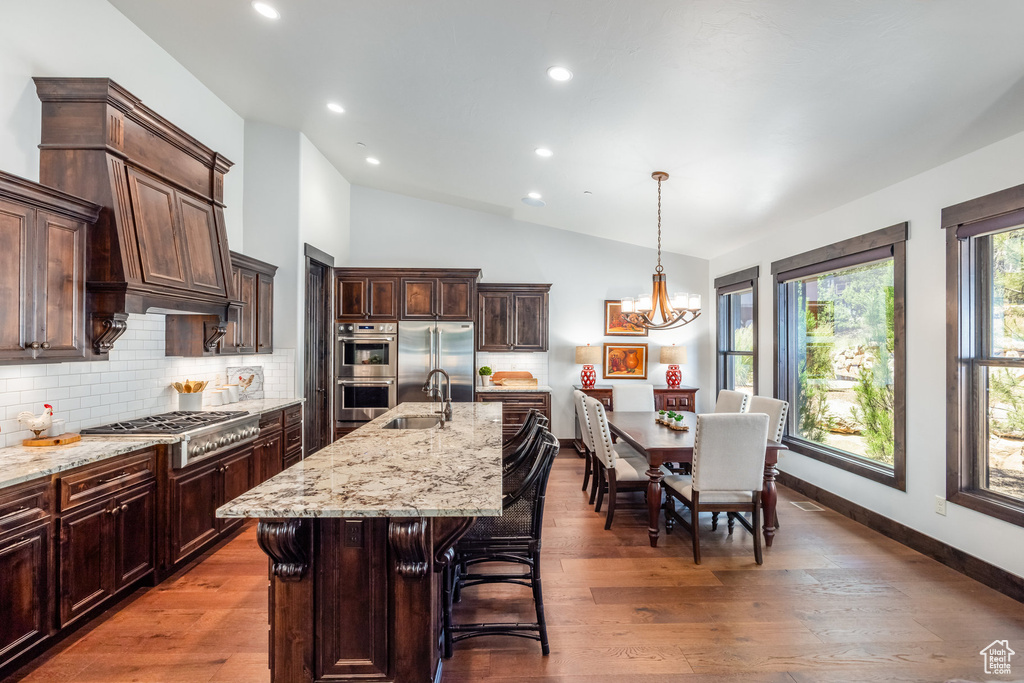 Kitchen with hanging light fixtures, an island with sink, appliances with stainless steel finishes, hardwood / wood-style floors, and tasteful backsplash