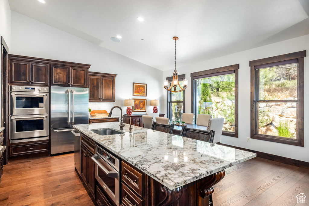 Kitchen featuring an island with sink, stainless steel appliances, lofted ceiling, and sink