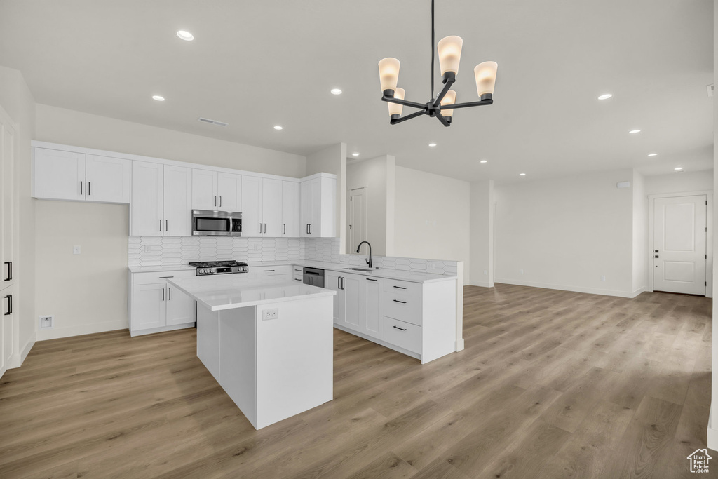 Kitchen with appliances with stainless steel finishes, white cabinetry, an inviting chandelier, light hardwood / wood-style flooring, and sink