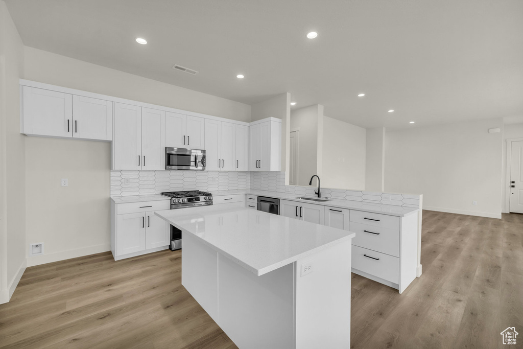 Kitchen featuring white cabinets, sink, a kitchen island, appliances with stainless steel finishes, and light wood-type flooring