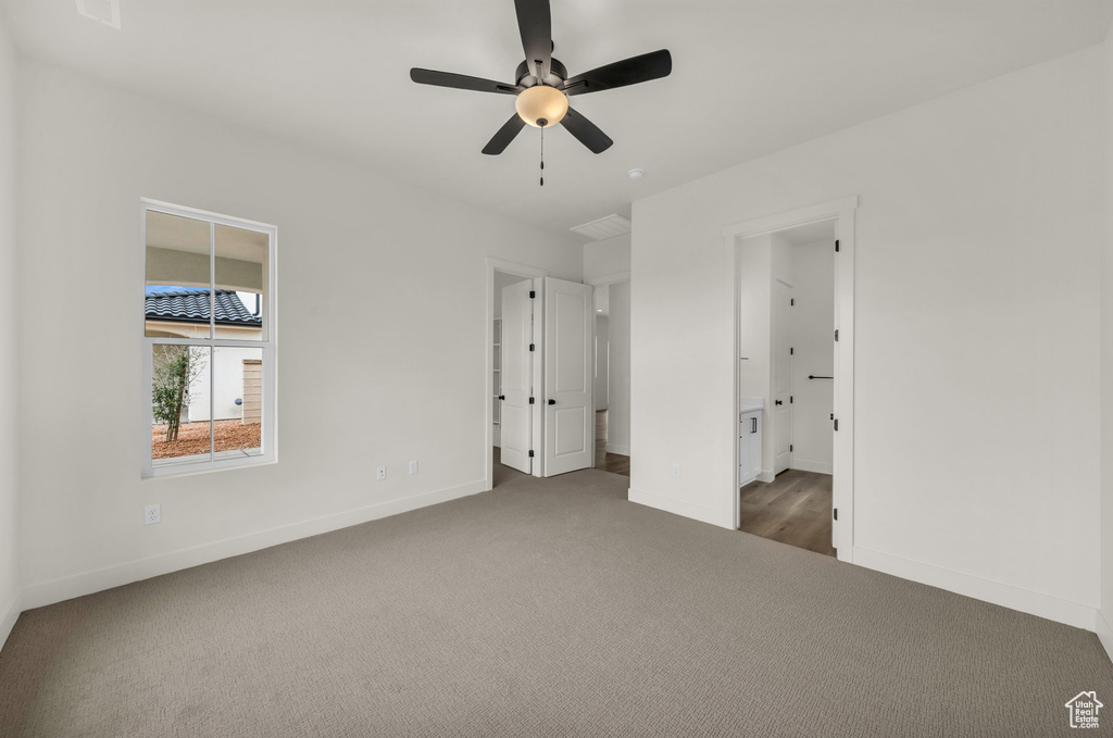 Unfurnished bedroom with ceiling fan, ensuite bath, and dark colored carpet