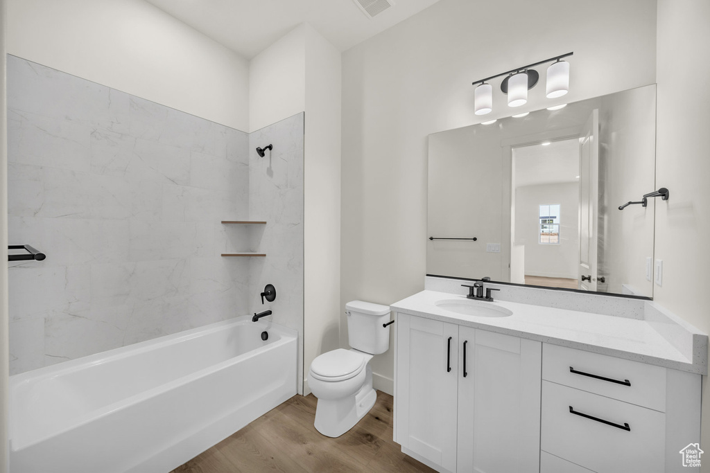 Full bathroom featuring wood-type flooring, tiled shower / bath combo, vanity, and toilet