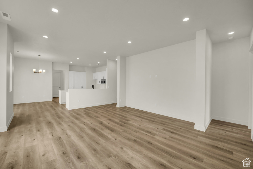 Unfurnished living room featuring an inviting chandelier and light hardwood / wood-style floors