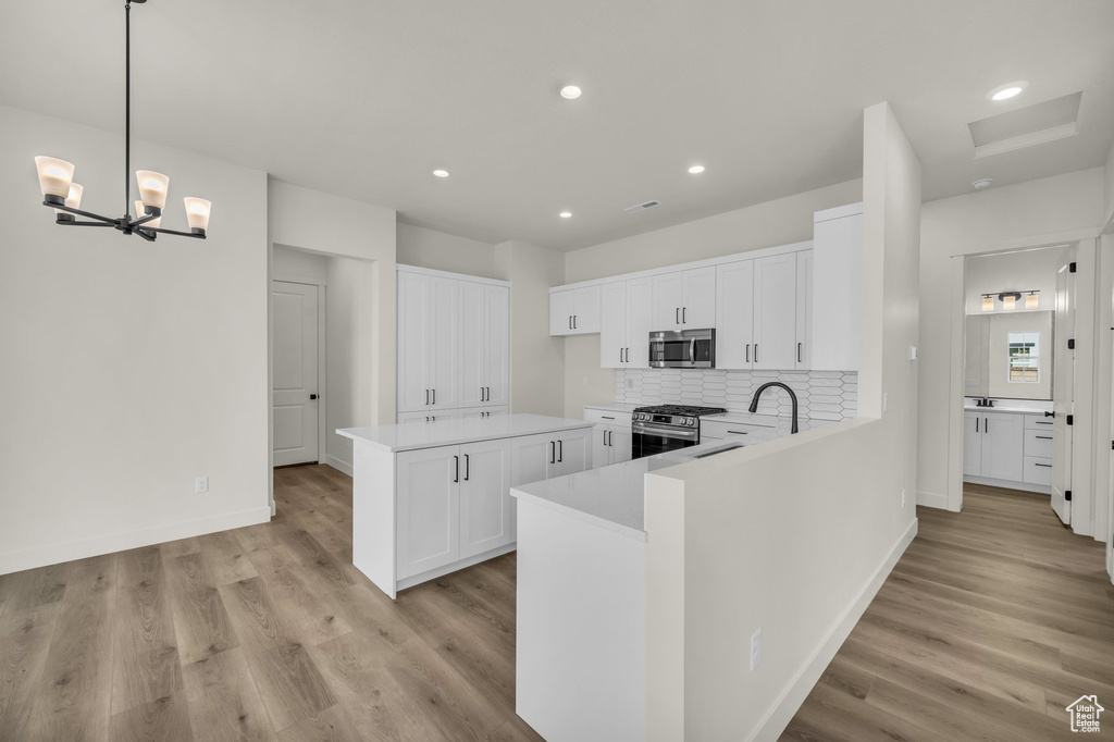 Kitchen with light hardwood / wood-style flooring, stainless steel appliances, white cabinetry, and hanging light fixtures