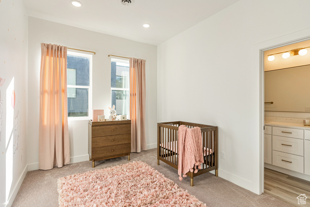 Bedroom with connected bathroom, light carpet, and a crib