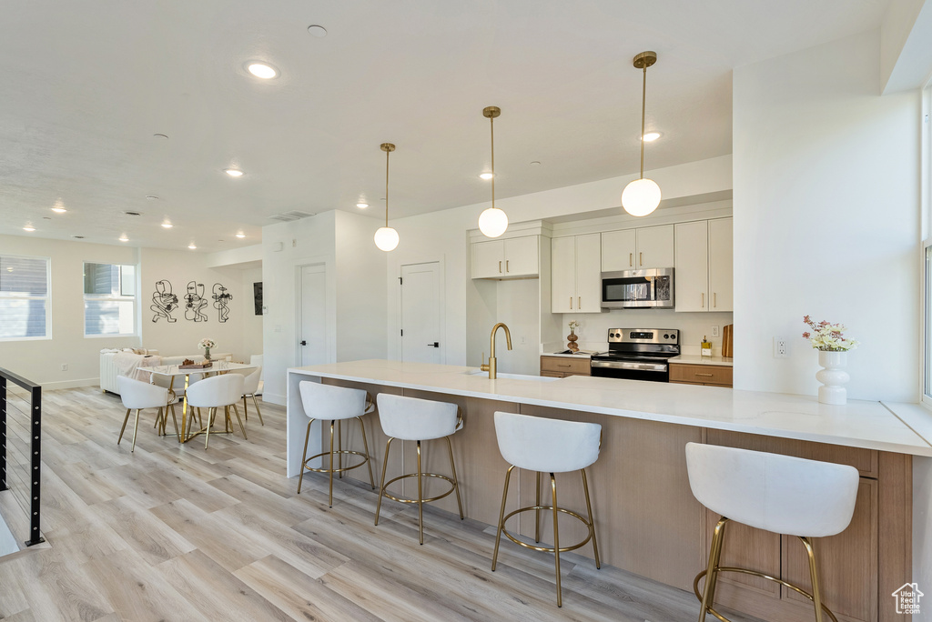 Kitchen with stainless steel appliances, sink, decorative light fixtures, white cabinets, and light hardwood / wood-style floors