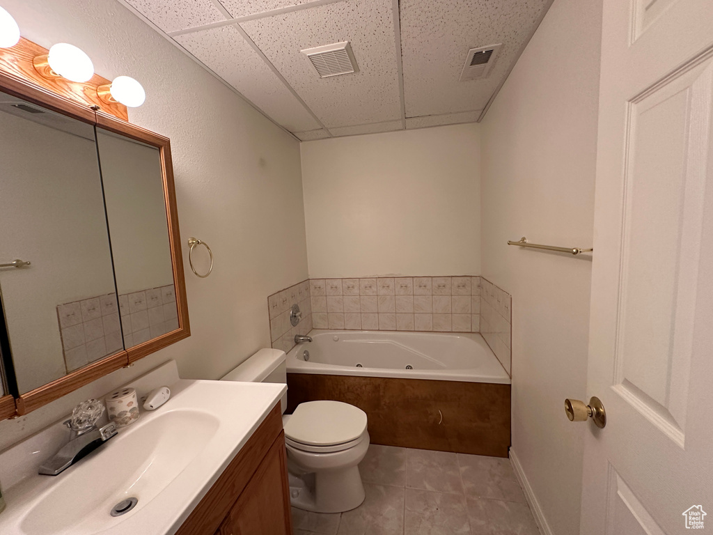 Bathroom with tile flooring, tiled bath, toilet, and a drop ceiling