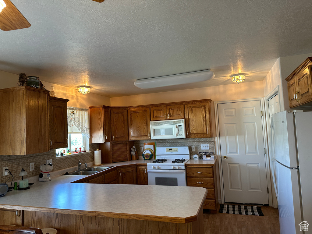 Kitchen featuring kitchen peninsula, tasteful backsplash, white appliances, sink, and hardwood / wood-style flooring