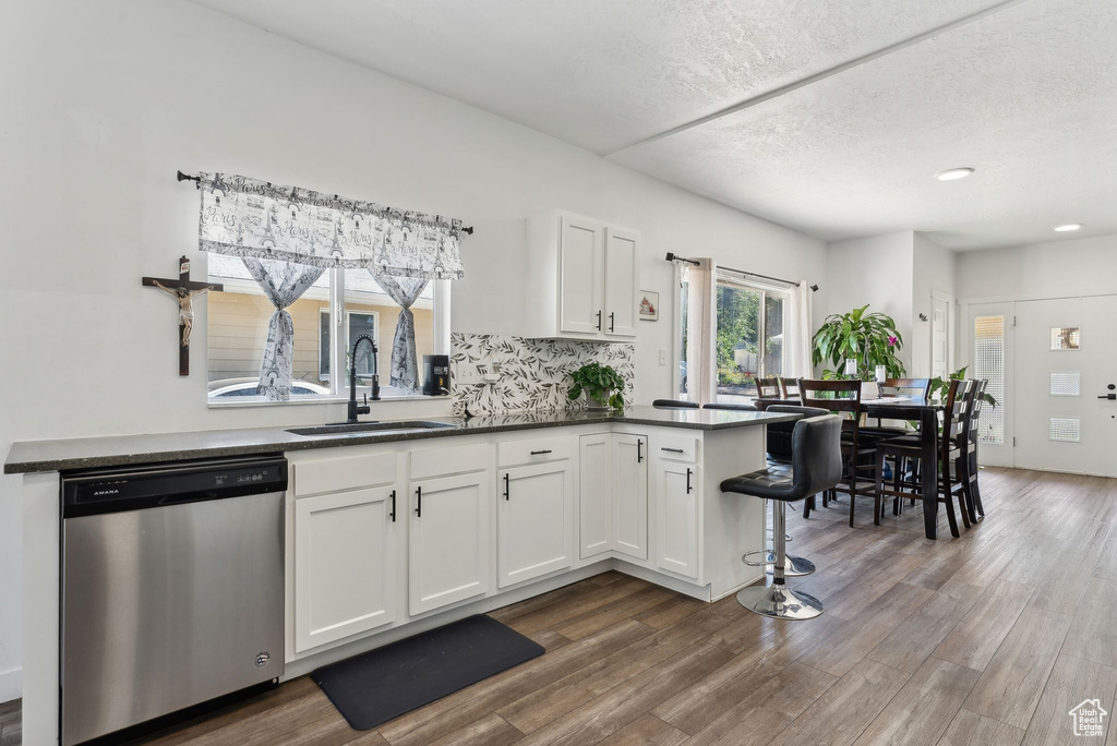 Kitchen featuring white cabinets, kitchen peninsula, dishwasher, dark wood-type flooring, and sink