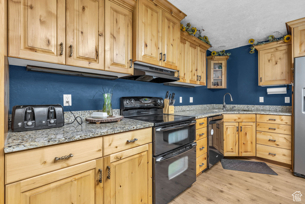 Kitchen featuring a textured ceiling, light hardwood / wood-style flooring, appliances with stainless steel finishes, light stone counters, and sink