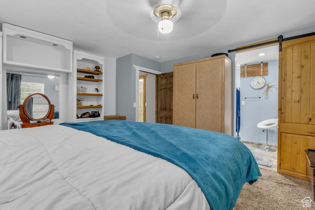 Carpeted bedroom with a barn door, ceiling fan, and ensuite bath