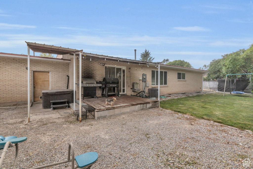 Back of property featuring a deck, a lawn, and a trampoline