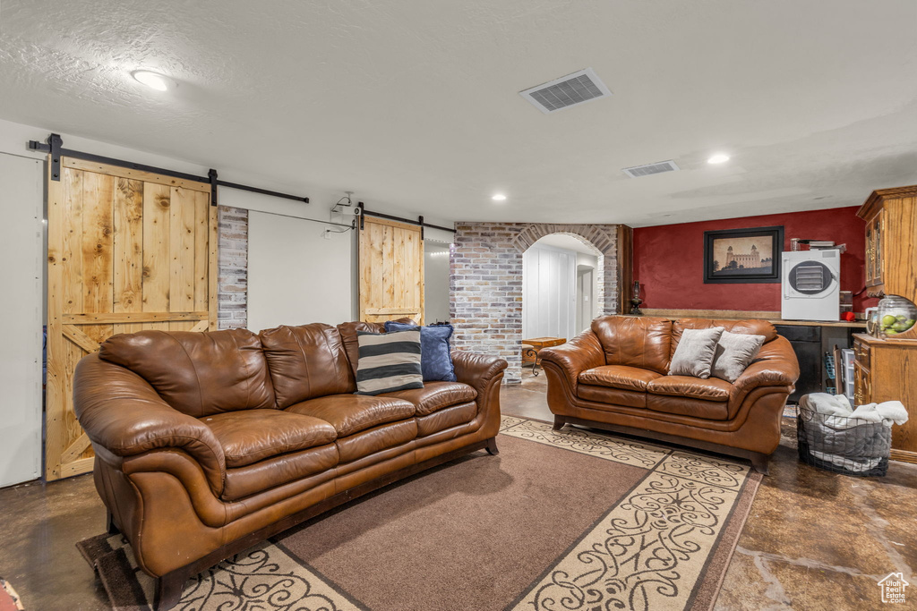 Living room featuring a barn door, a textured ceiling, and brick wall