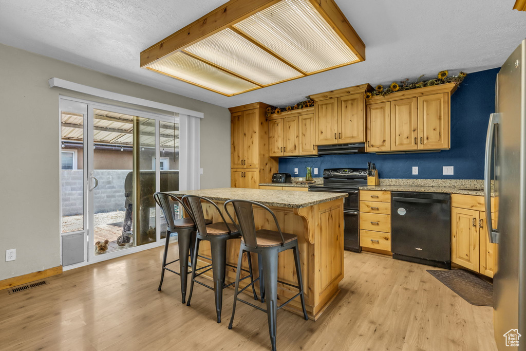 Kitchen featuring a center island, light hardwood / wood-style floors, light stone countertops, black appliances, and a kitchen bar