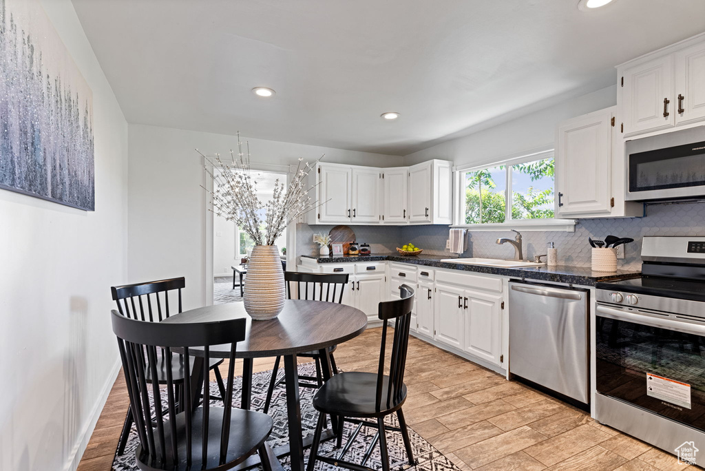 Kitchen with appliances with stainless steel finishes, light hardwood / wood-style flooring, tasteful backsplash, white cabinets, and sink