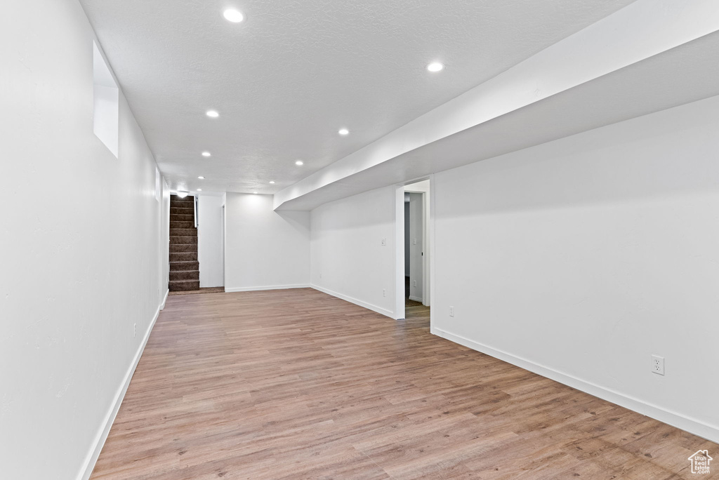 Basement with brick wall and light hardwood / wood-style flooring