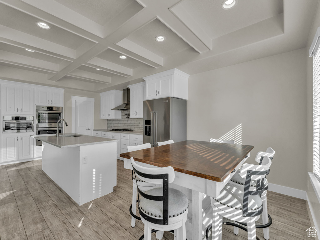 Kitchen with a sink, wall chimney exhaust hood, stainless steel appliances, backsplash, and coffered ceiling