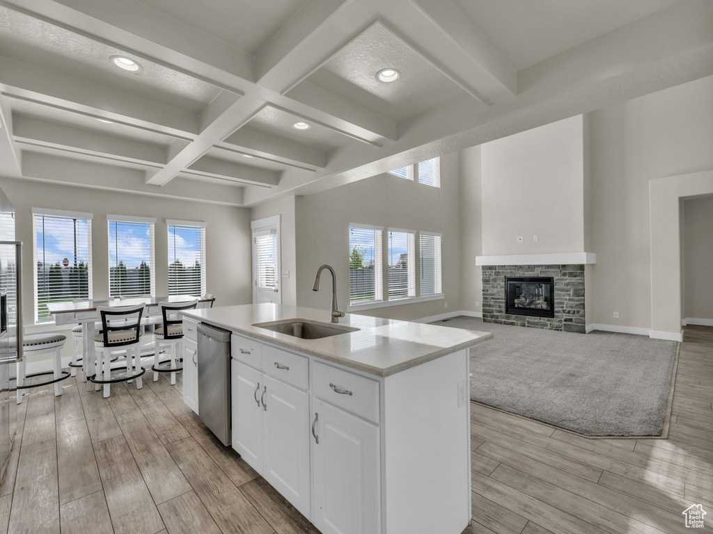 Kitchen with stainless steel dishwasher, a center island with sink, a sink, coffered ceiling, and white cabinetry
