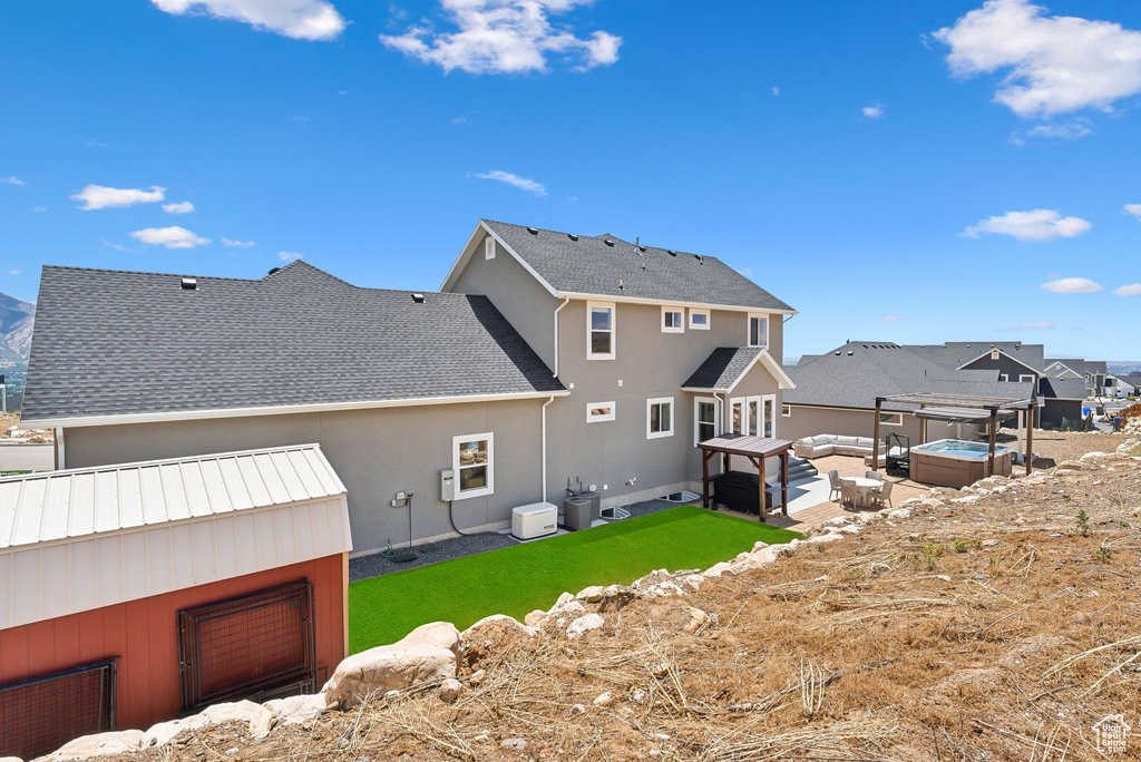 Back of property with a hot tub and a lawn