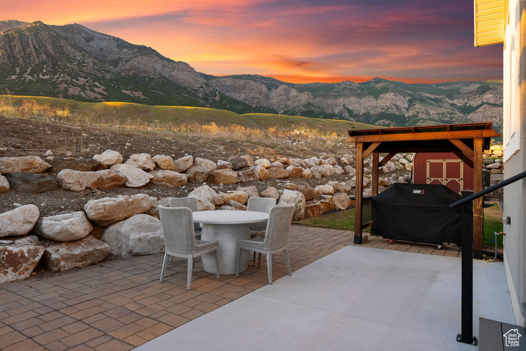 Patio terrace at dusk featuring a mountain view, a shed, and area for grilling