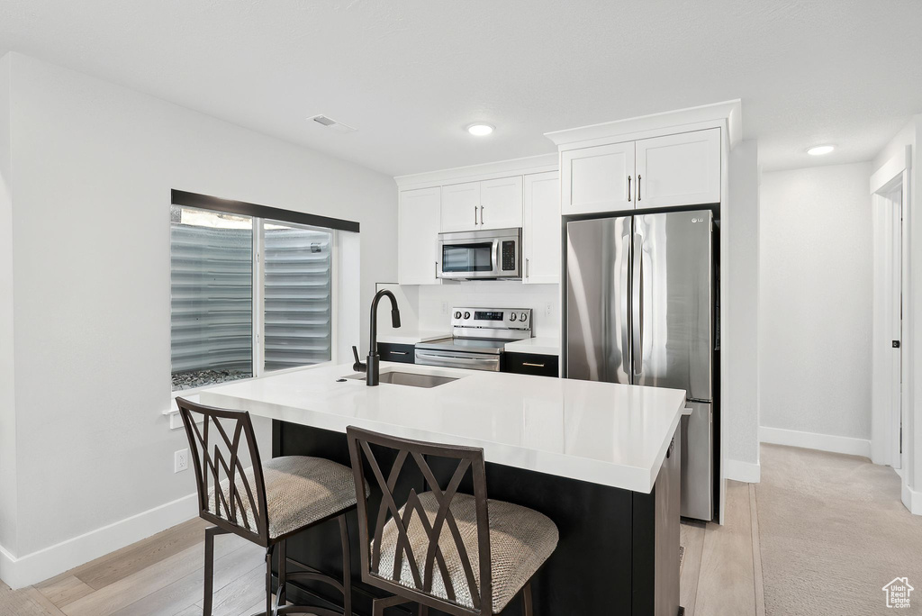 Kitchen with an island with sink, white cabinetry, sink, and stainless steel appliances