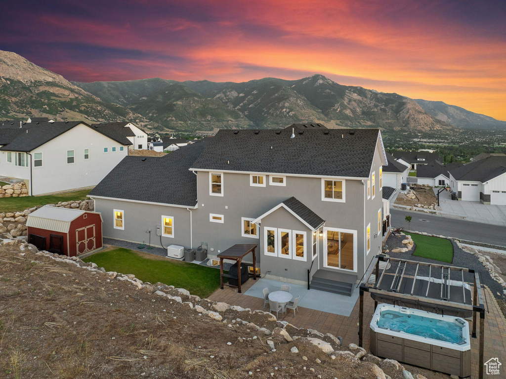 Back house at dusk with a patio area, a mountain view, a hot tub, central air condition unit, and a shed