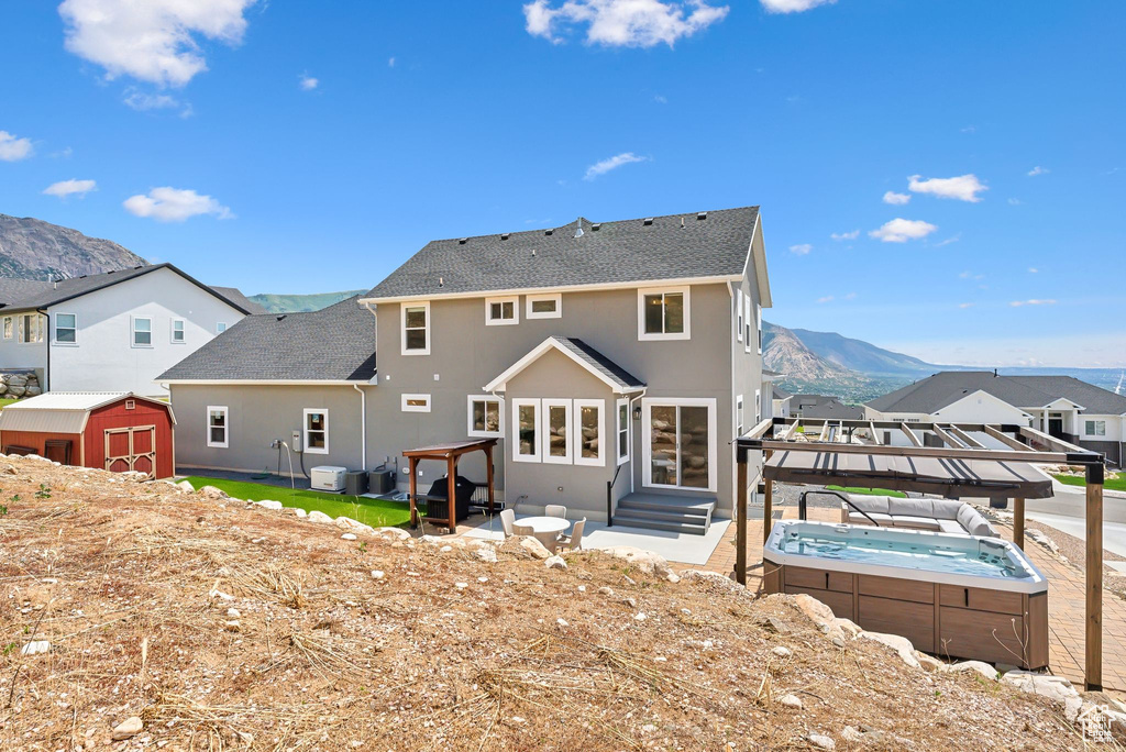 Rear view of property featuring a mountain view, a storage shed, and a hot tub