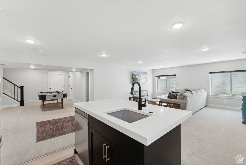 Kitchen with an island with sink, sink, dishwasher, and light carpet